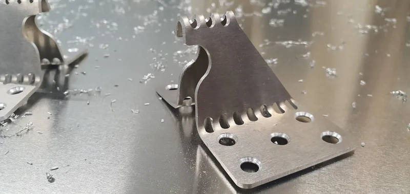 Folded aluminium brackets with slotted edges among swarf on the machine bed.